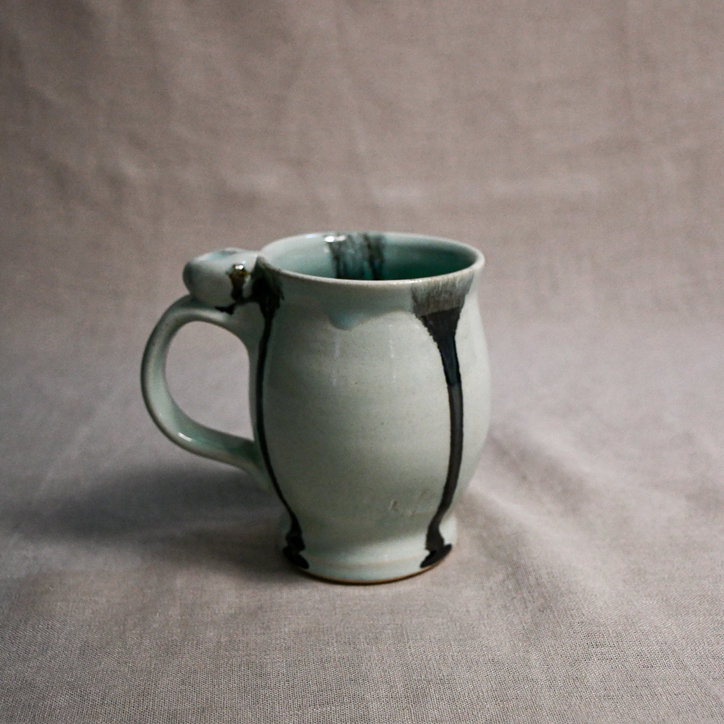 Pale blue handmade pottery mug with black drips from the 5th Buffalo collection by Leigh Art