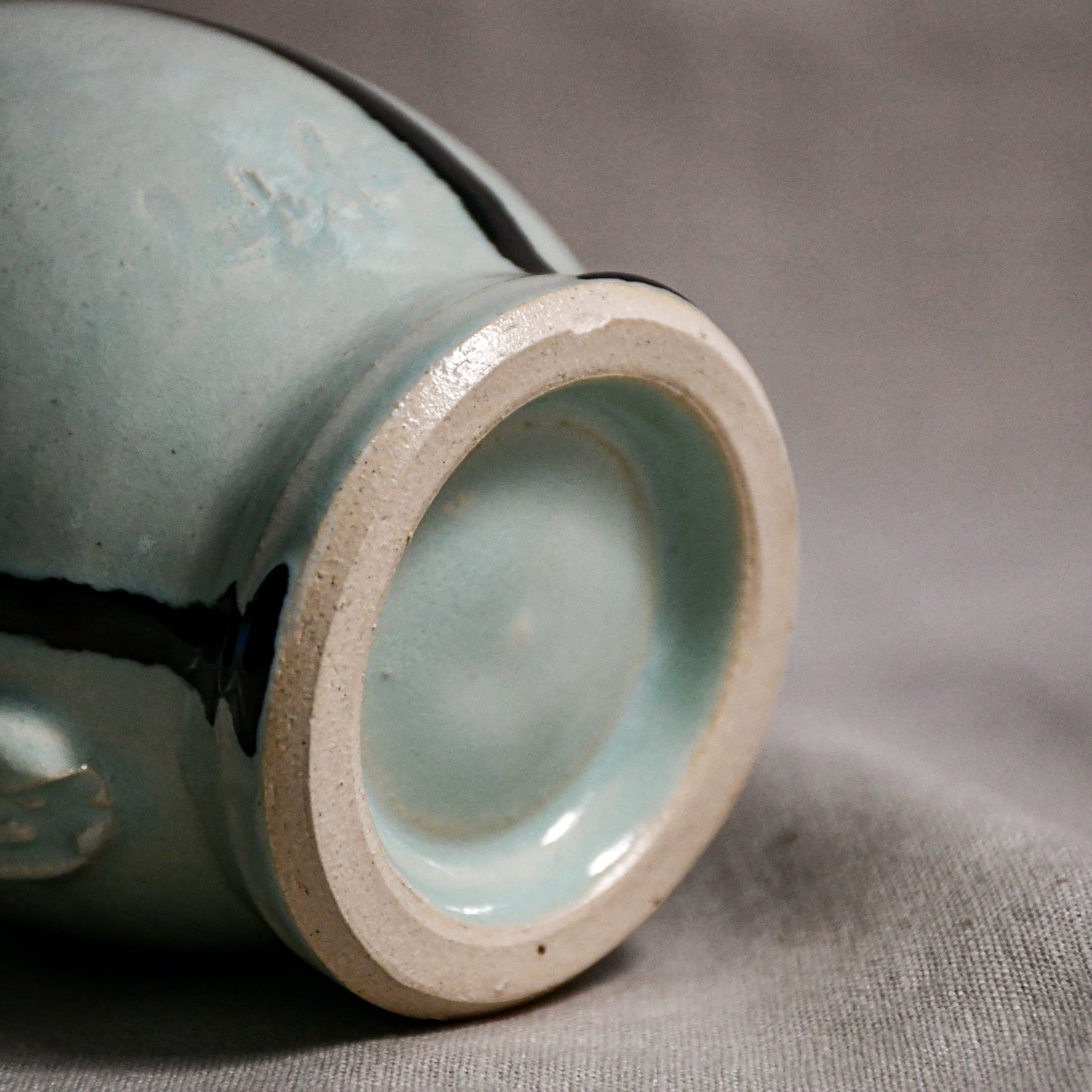 Bottom view close up of pale blue handmade mug showing trimmed fired ceramic foot and texture.