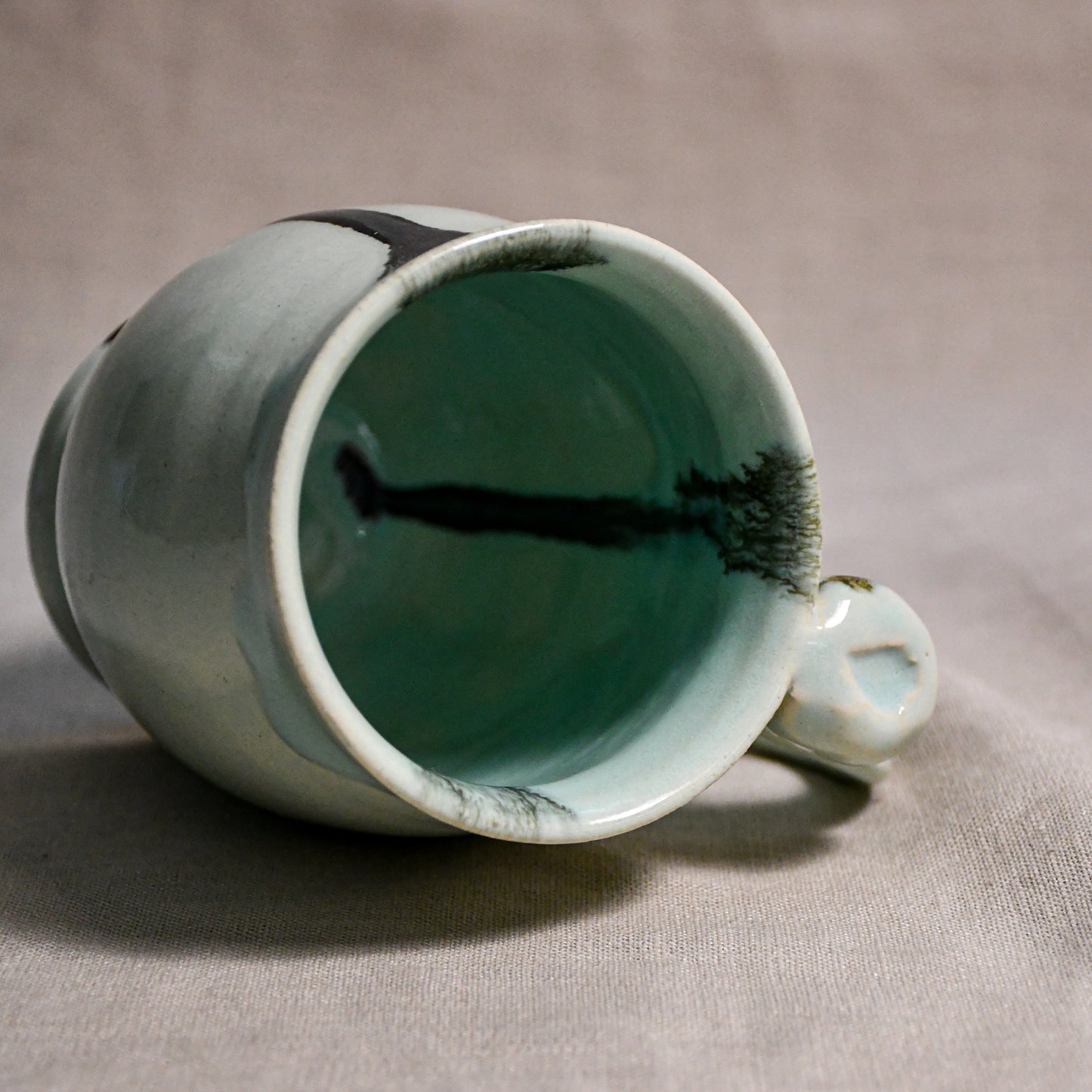 Close up of rim and handle of pale blue handmade mug with stamped thumbrest, black drips and showing texture