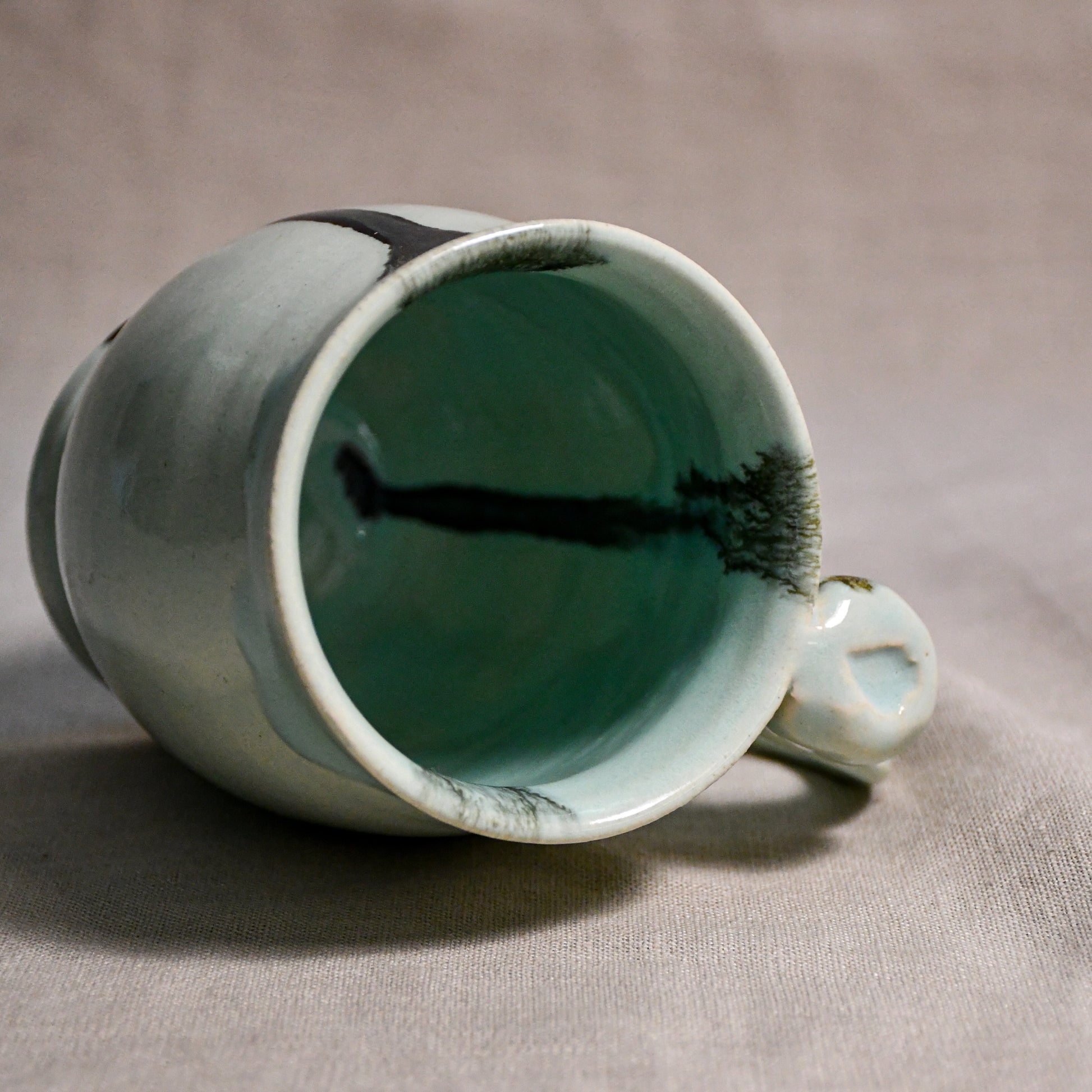 Close up of rim and handle of pale blue handmade mug with stamped thumbrest, black drips and showing texture