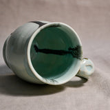 Close up of rim and handle of pale blue handmade mug with stamped thumbrest, black drips and showing texture