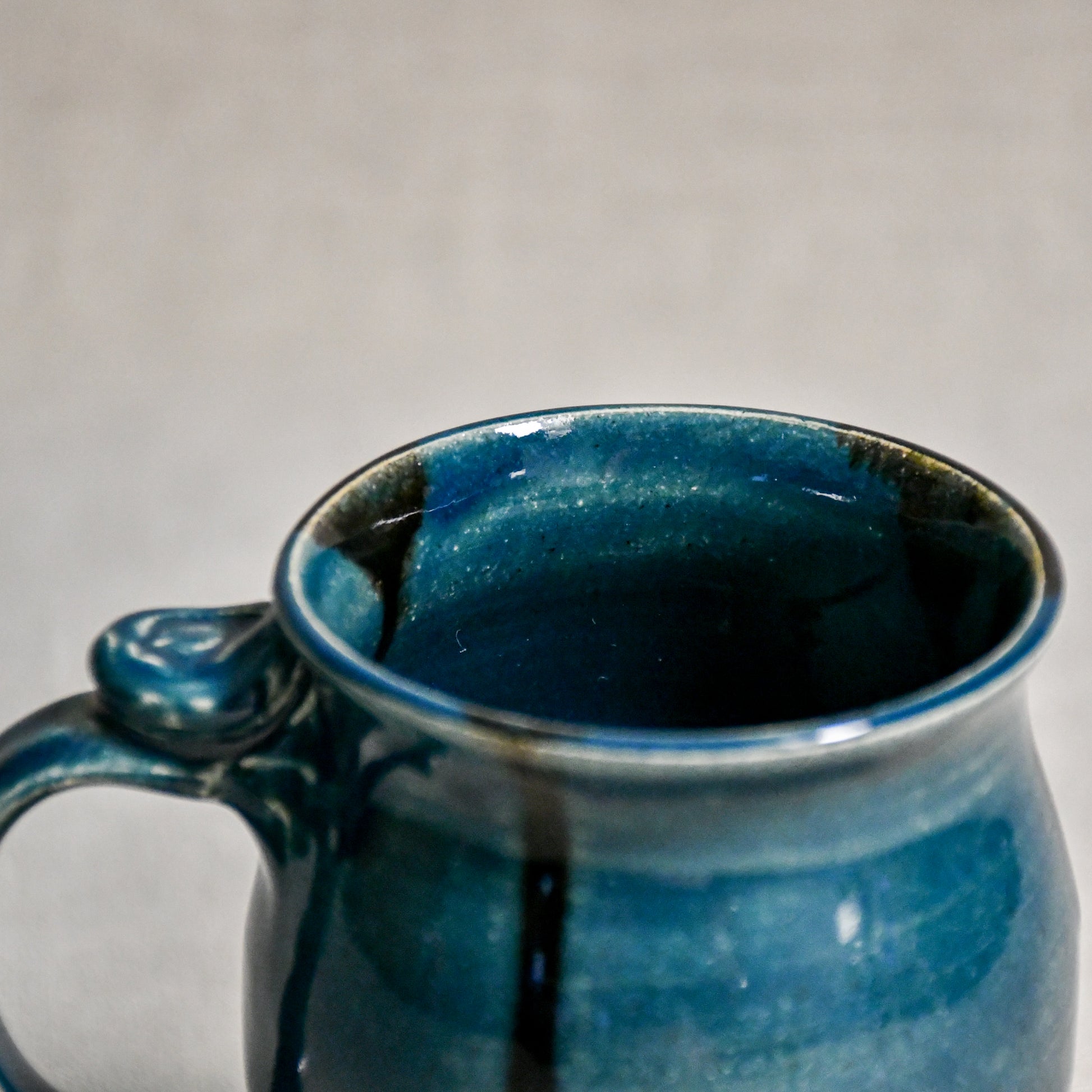 Close up of rim and handle of dark teal handmade mug with stamped thumbrest, black drips and showing texture