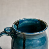 Close up of rim and handle of dark teal handmade mug with stamped thumbrest, black drips and showing texture