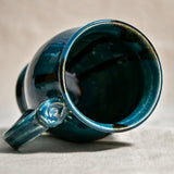 Close up of rim and handle of dark teal handmade mug with stamped thumbrest, black drips and showing texture