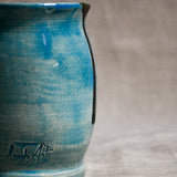 Close up of a turquoise handmade mug showing texture and black drips.