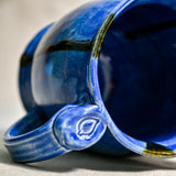 Close up of rim and handle of blue handmade mug with stamped thumbrest, black drips and showing texture