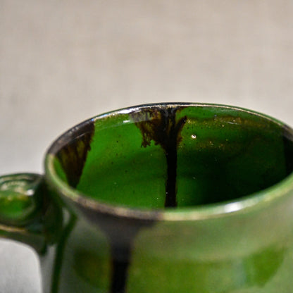 Close up of rim and interior of green handmade mug with stamped thumbrest, black drips and showing texture