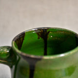 Close up of rim and interior of green handmade mug with stamped thumbrest, black drips and showing texture