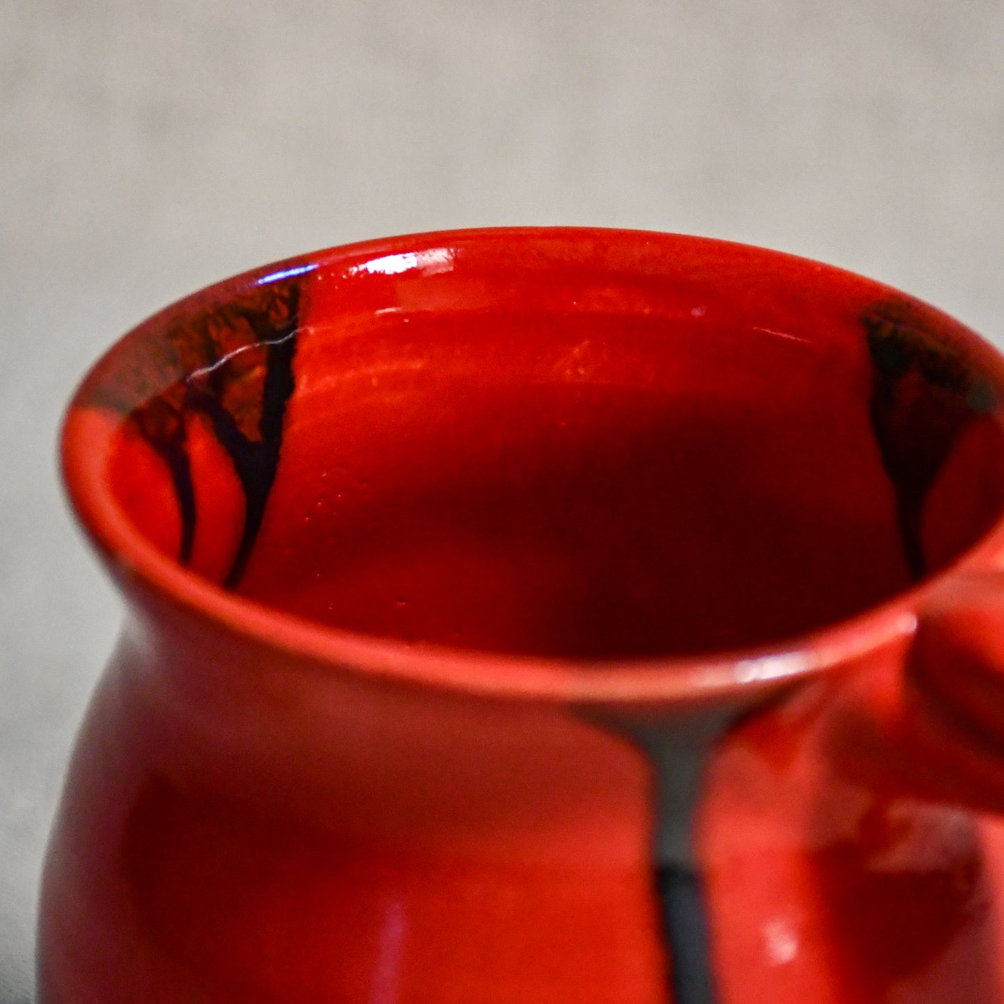 Close up of rim and interior of red handmade mug with black drips and showing texture