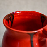 Close up of rim and interior of red handmade mug with black drips and showing texture