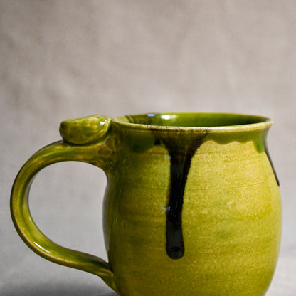 Close up of a lime green handmade mug showing texture and black drips.