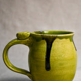 Close up of a lime green handmade mug showing texture and black drips.