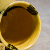 Close up of rim and interior of yellow handmade mug with black drips and showing texture and crazing.