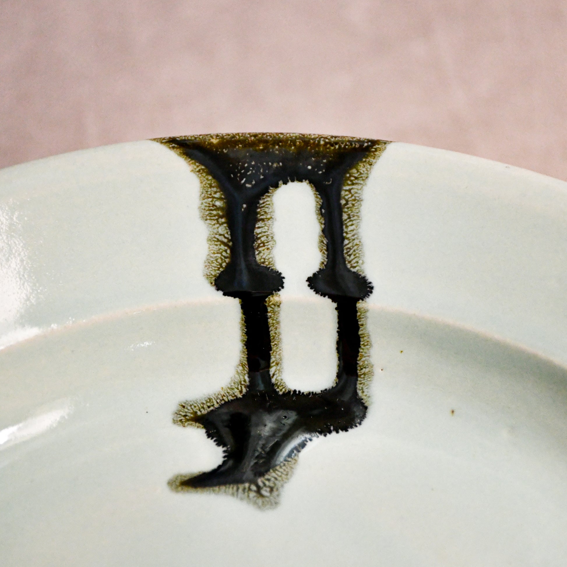 Close up of a pale blue ceramic dinner plate showing black drips and texture