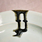 Close up of a pale blue ceramic dinner plate showing black drips and texture