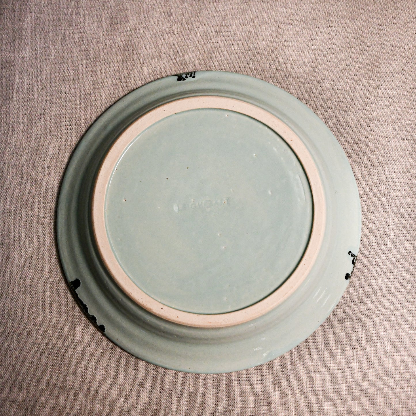 Bottom view of a pale blue ceramic dinner plate showing exposed stoneware clay and texture