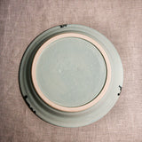 Bottom view of a pale blue ceramic dinner plate showing exposed stoneware clay and texture