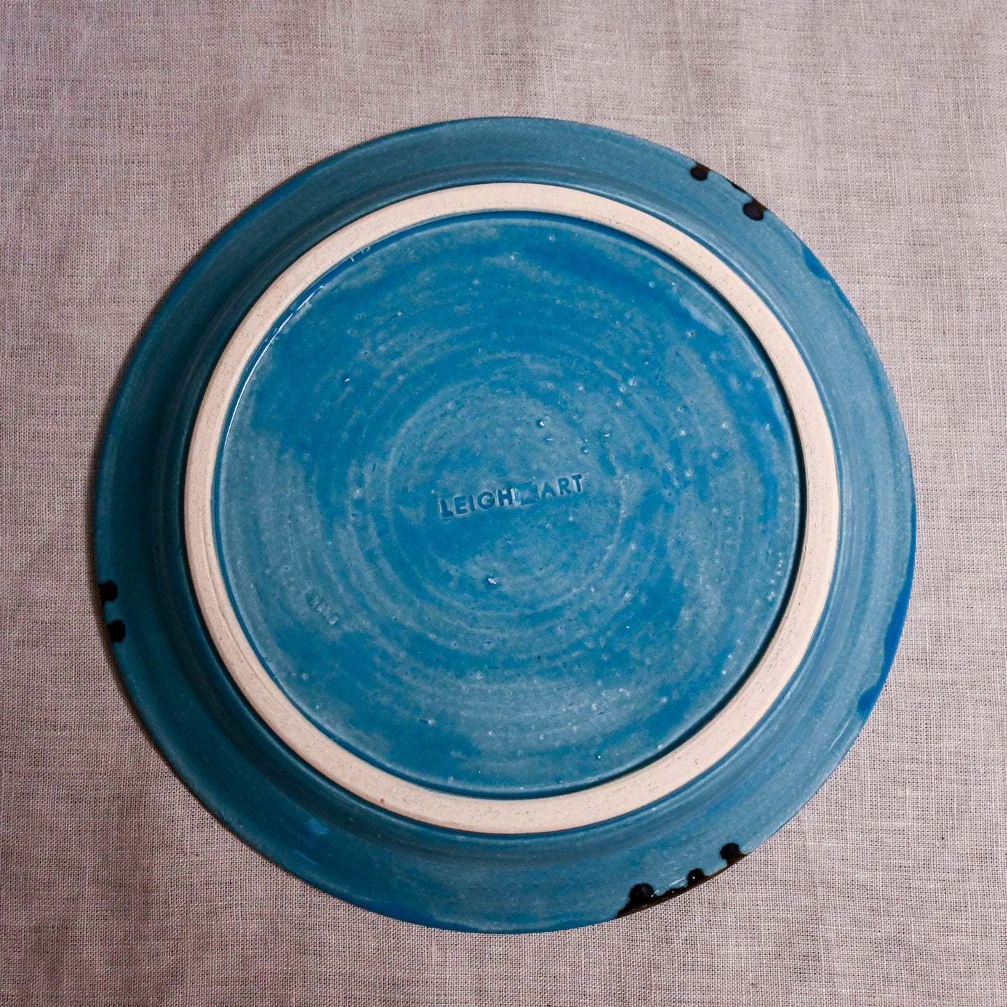 Bottom view of a turquoise ceramic dinner plate showing exposed stoneware clay and texture