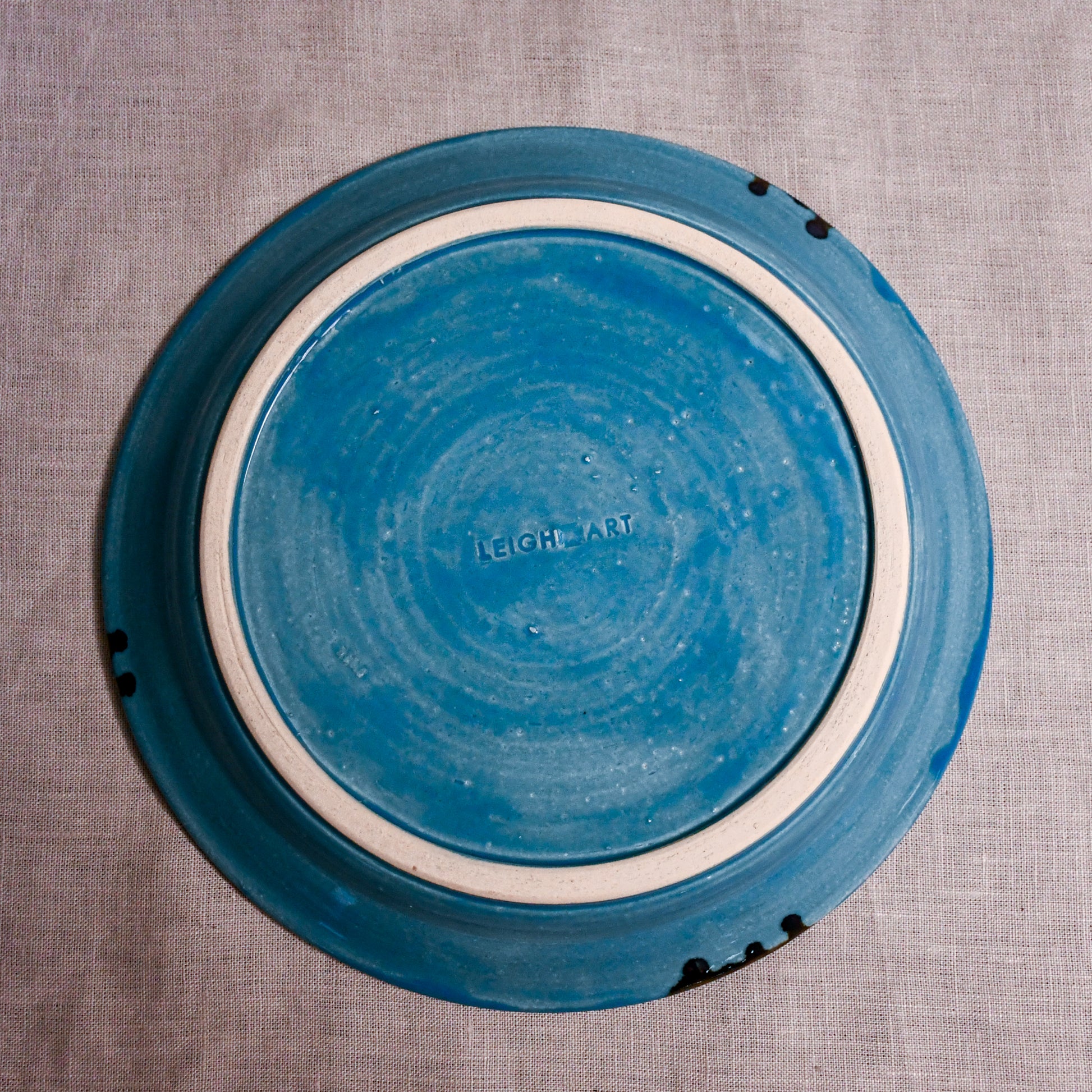 Bottom view of a turquoise ceramic dinner plate showing exposed stoneware clay and texture