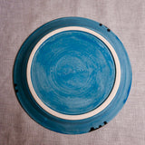 Bottom view of a turquoise ceramic dinner plate showing exposed stoneware clay and texture
