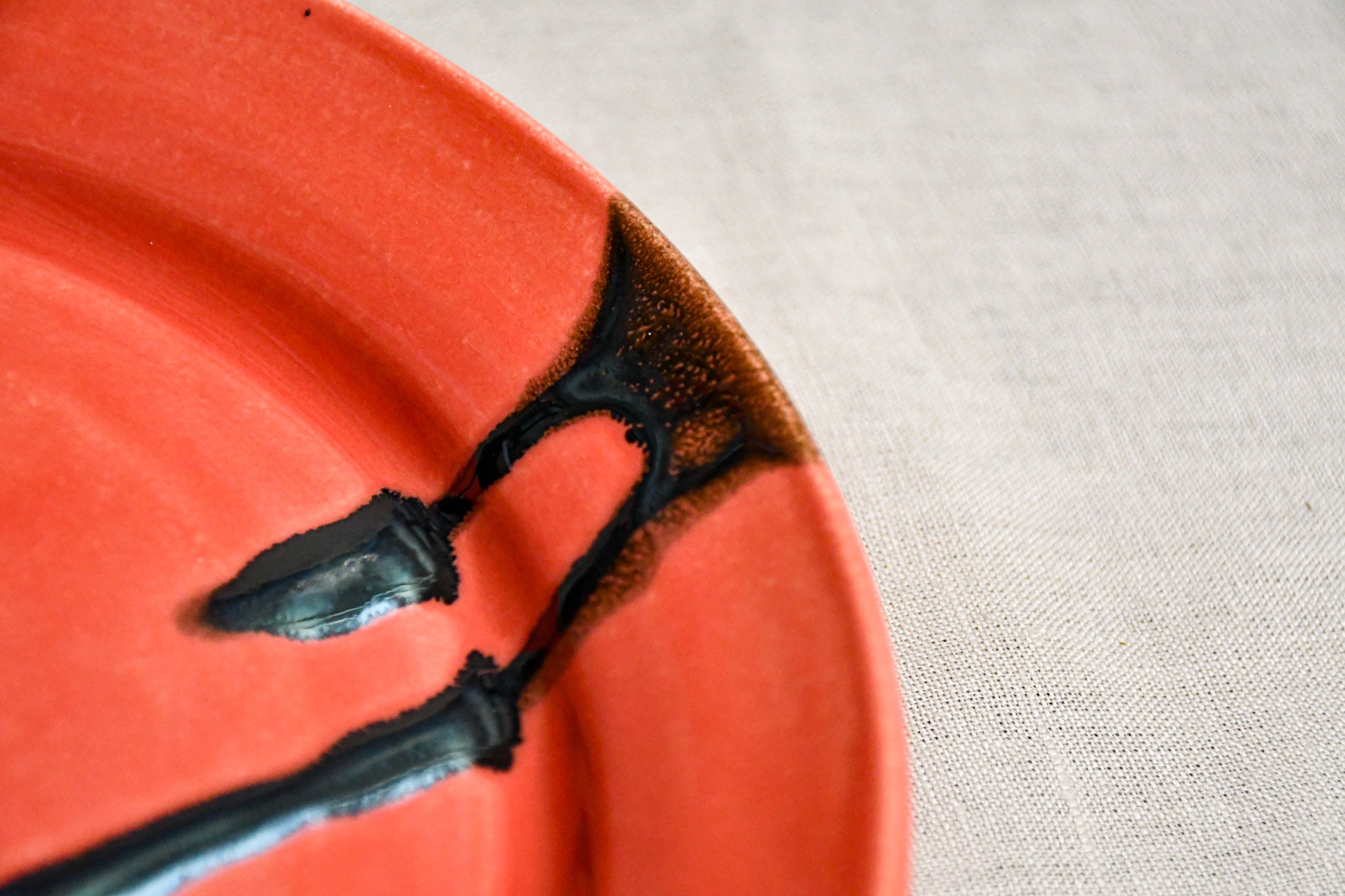 Close up of a coral ceramic dinner plate showing black drips and texture