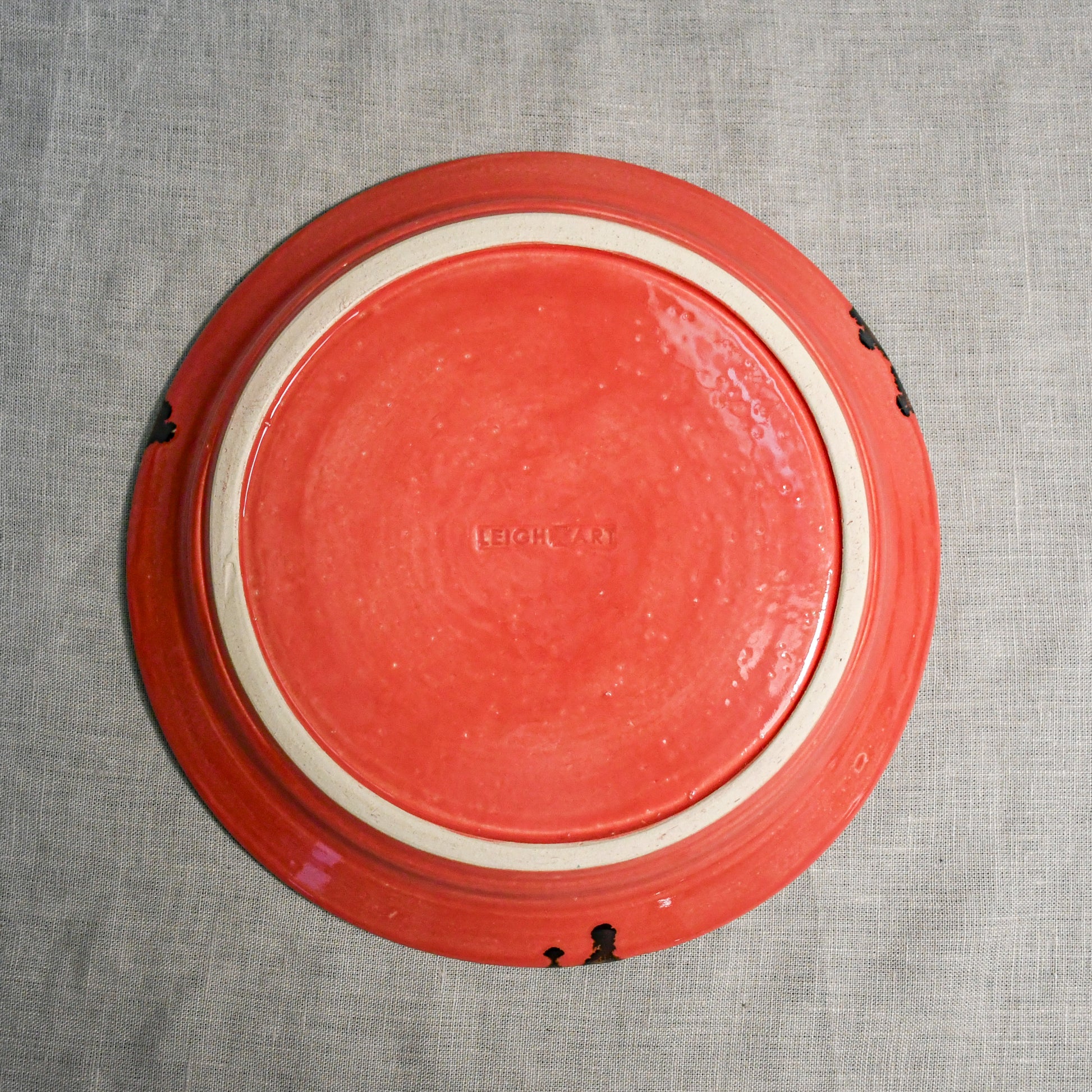 Bottom view of a coral ceramic dinner plate showing exposed stoneware clay and texture