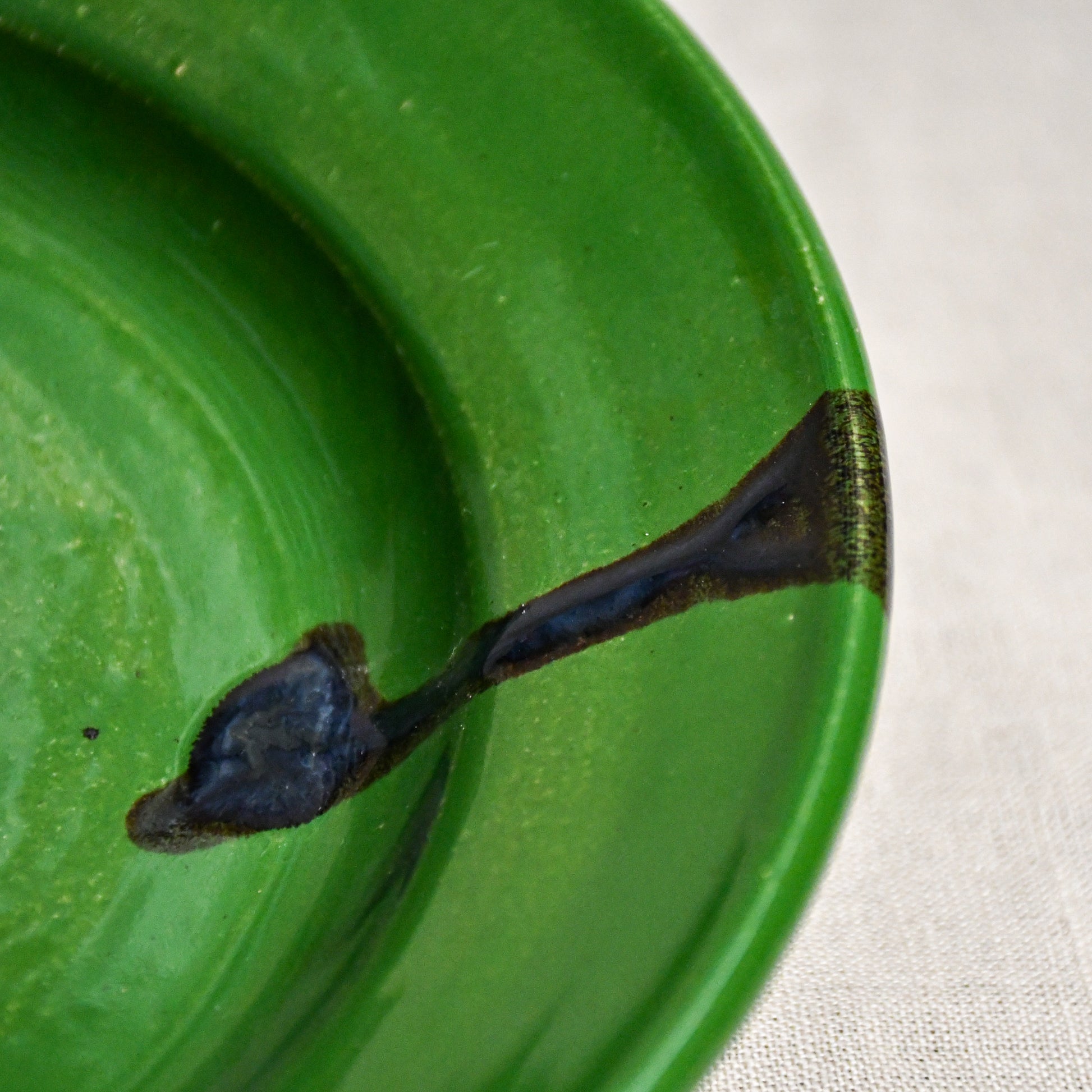 Close up of a green ceramic dinner plate showing black drips and texture