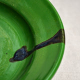 Close up of a green ceramic dinner plate showing black drips and texture