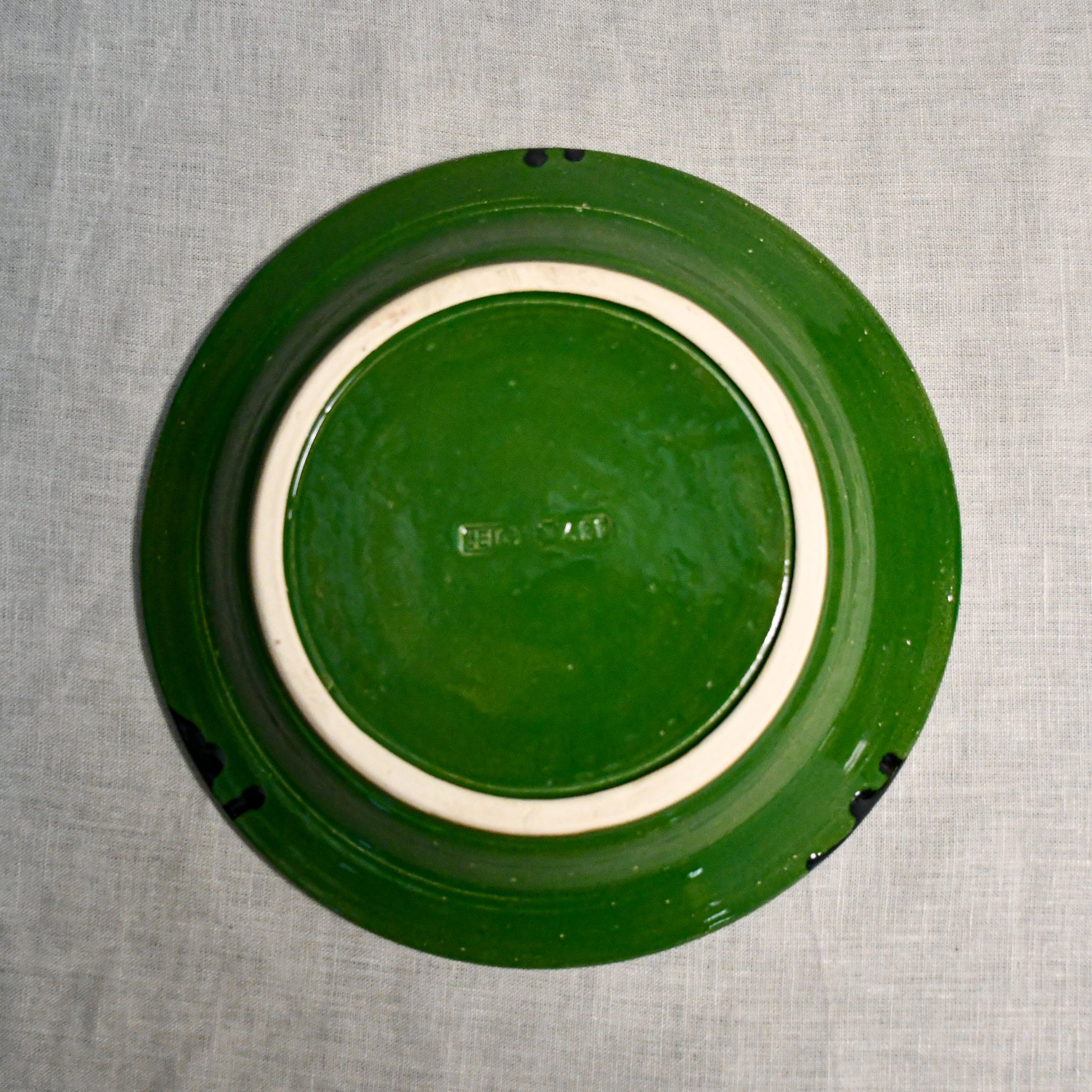 Bottom view of a green ceramic dinner plate showing exposed stoneware clay and texture