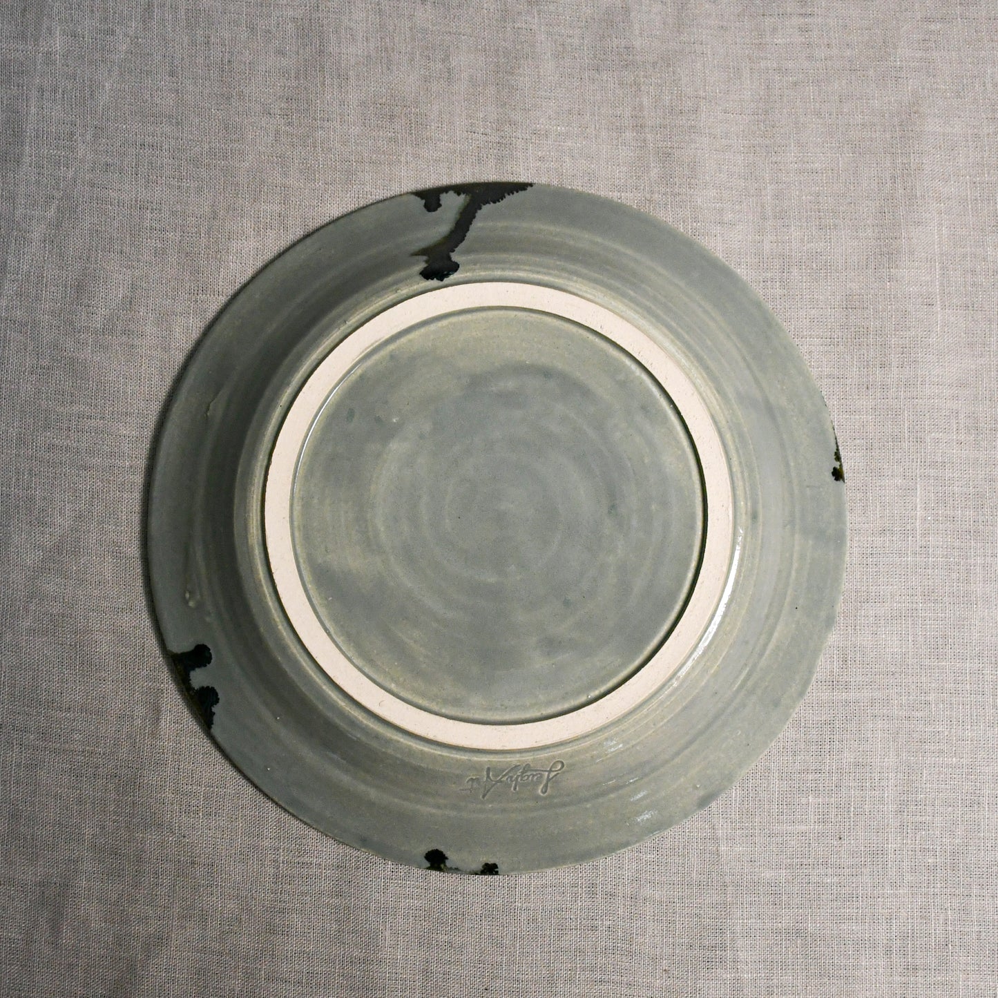 Bottom view of a grey ceramic dinner plate showing exposed stoneware clay and texture