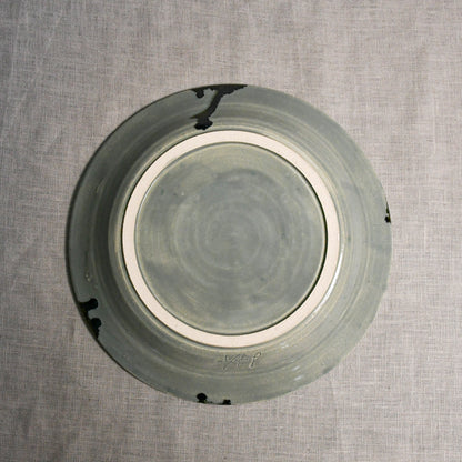 Bottom view of a grey ceramic dinner plate showing exposed stoneware clay and texture