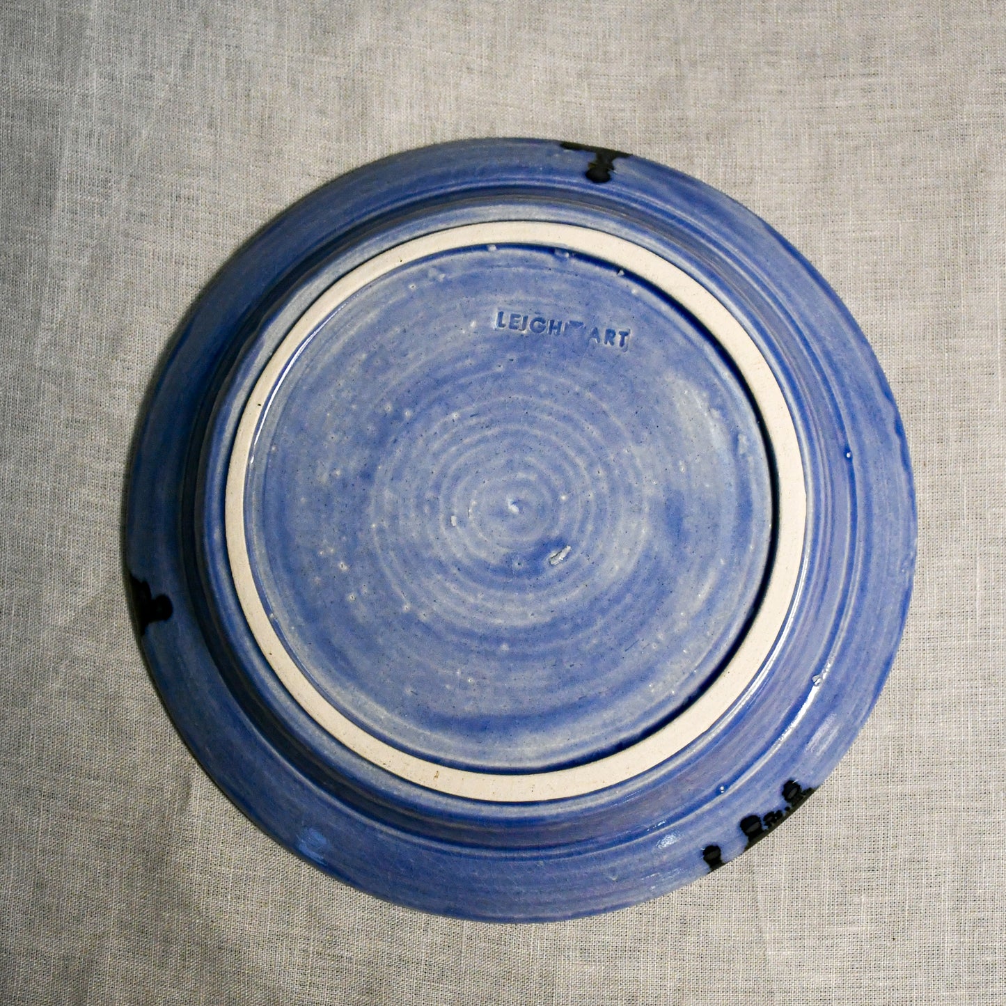 Bottom view of a purple ceramic dinner plate showing exposed stoneware clay and texture