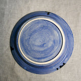 Bottom view of a purple ceramic dinner plate showing exposed stoneware clay and texture