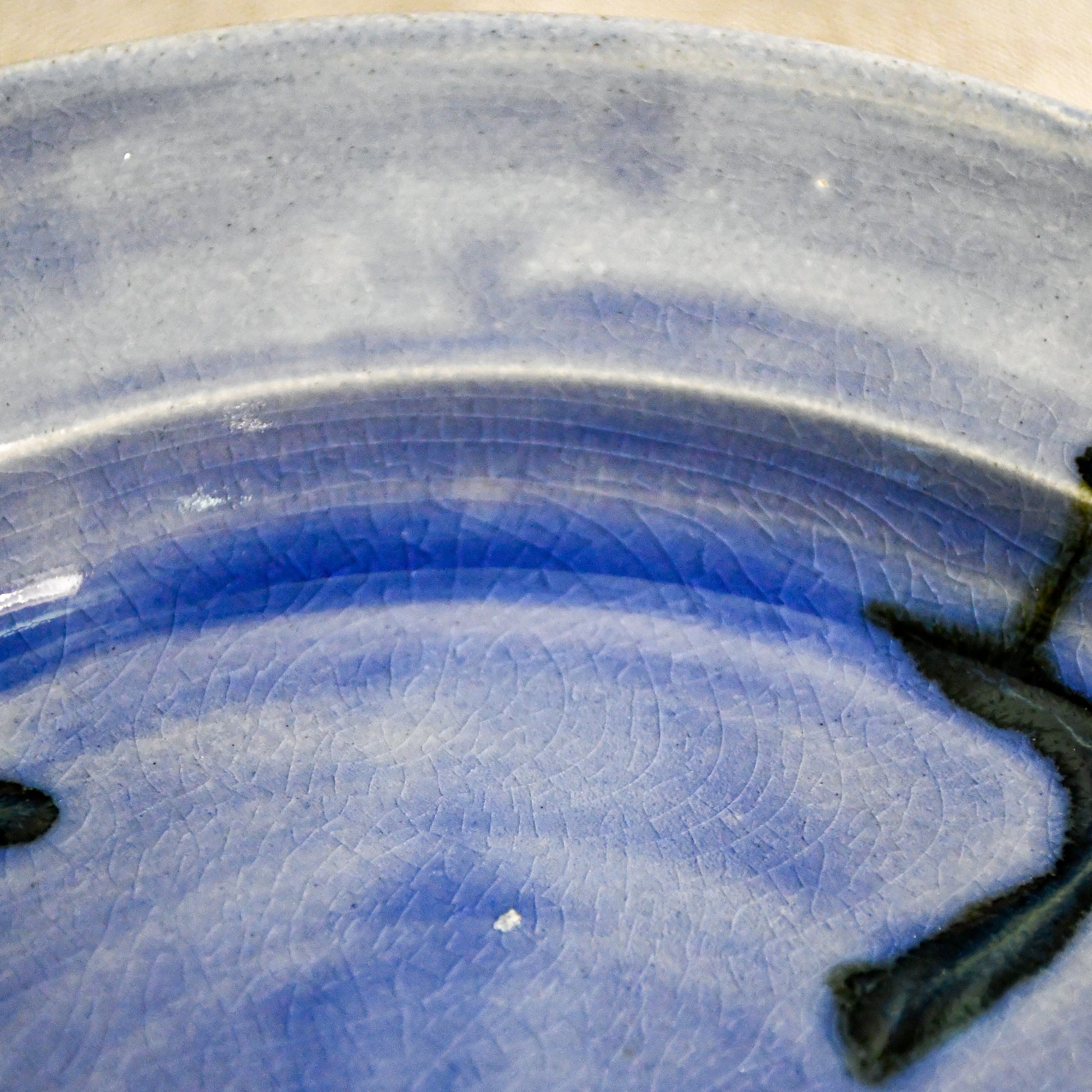 Close-up of black glaze drips and crazing on a purple handmade wheelthrown pottery dinner plate
