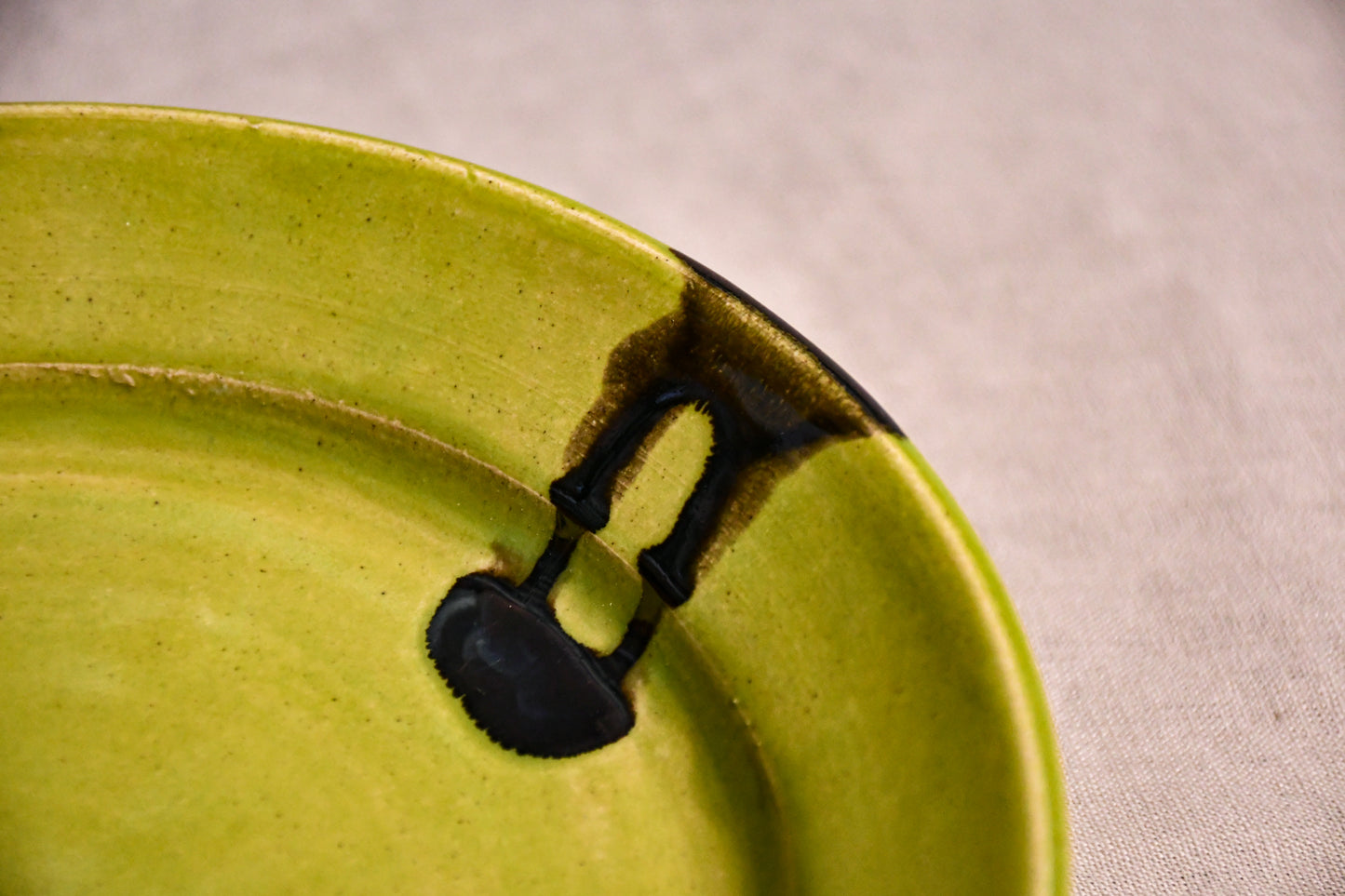 Close up of a lime green ceramic dinner plate showing black drips and texture