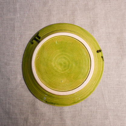 Bottom view of a lime green ceramic dinner plate showing exposed stoneware clay and texture