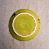 Bottom view of a lime green ceramic dinner plate showing exposed stoneware clay and texture