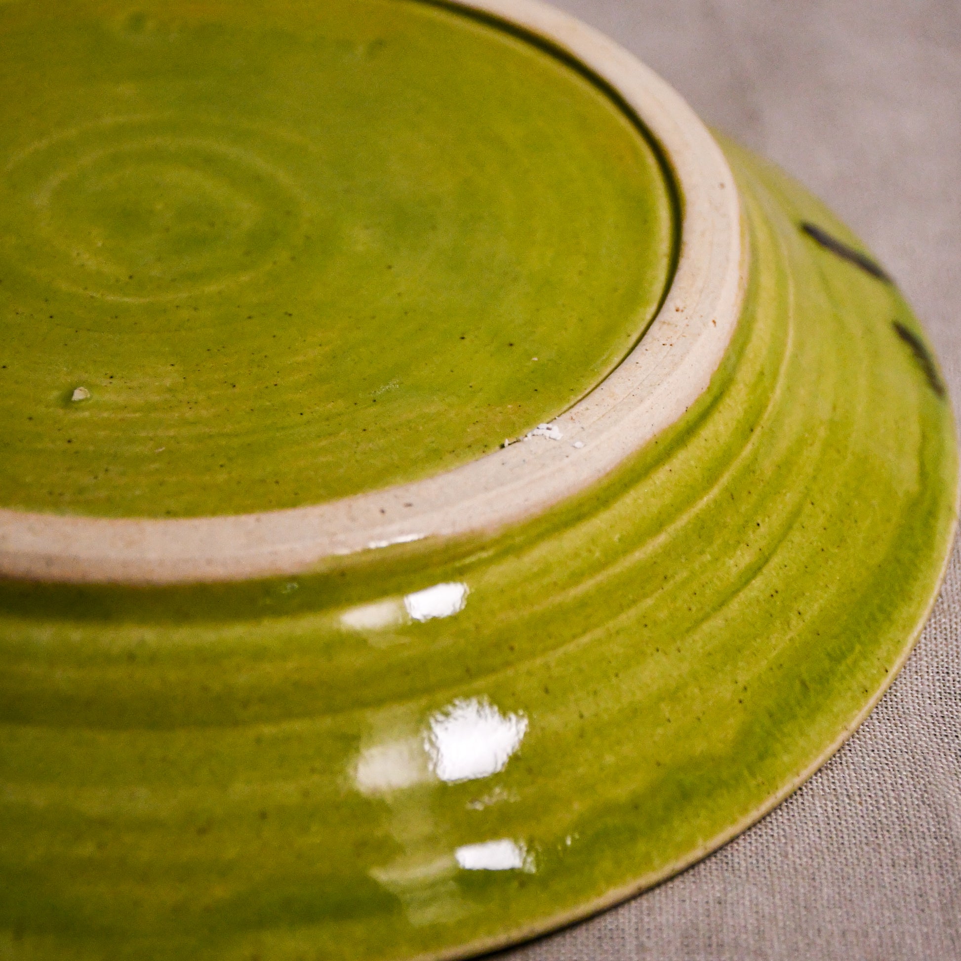 Close up of bottom of a lime green ceramic dinner plate showing exposed stoneware clay foot and texture