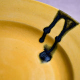 Close up of a yellow ceramic dinner plate showing black drips, texture, and crazing.