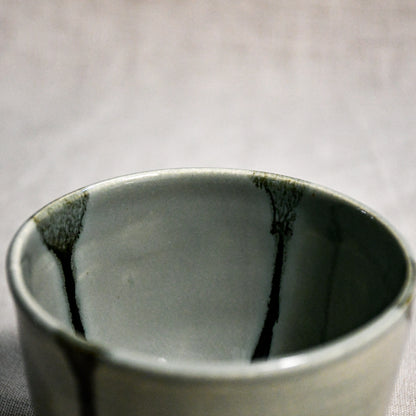 Close up of a grey handmade wheelthrown pottery salsa bowl from the 5th Buffalo collection by Leigh Art showing black drips and texture. 