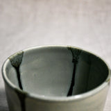 Close up of a grey handmade wheelthrown pottery salsa bowl from the 5th Buffalo collection by Leigh Art showing black drips and texture. 