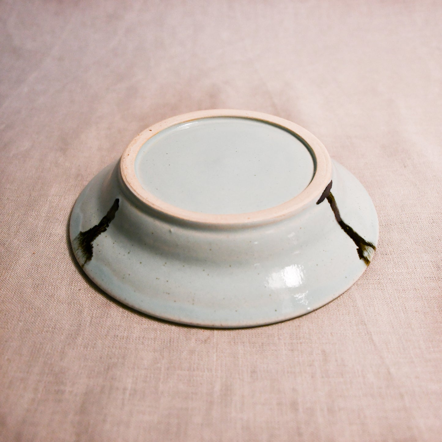 Close up of bottom of a pale blue ceramic saucer showing exposed stoneware clay foot and texture