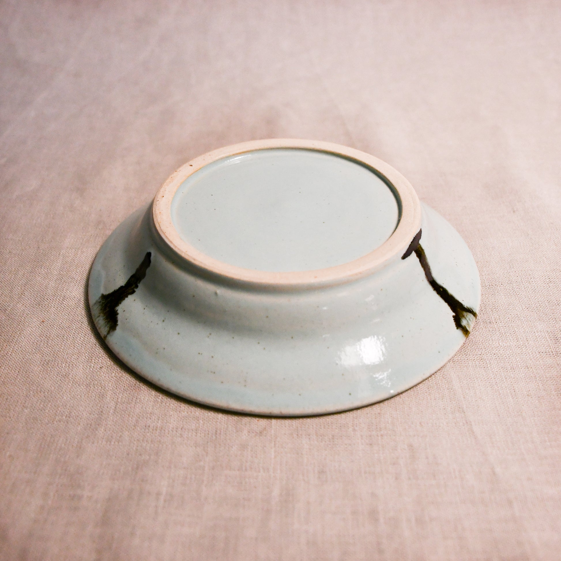 Close up of bottom of a pale blue ceramic saucer showing exposed stoneware clay foot and texture