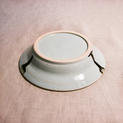 Close up of bottom of a pale blue ceramic saucer showing exposed stoneware clay foot and texture
