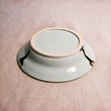 Close up of bottom of a pale blue ceramic saucer showing exposed stoneware clay foot and texture