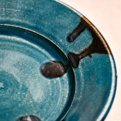 Close up of dark teal handmade wheelthrown pottery saucer with black drips from the 5th Buffalo collection by Leigh Art