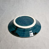 Close up of bottom of a dark teal ceramic saucer showing exposed stoneware clay foot and texture