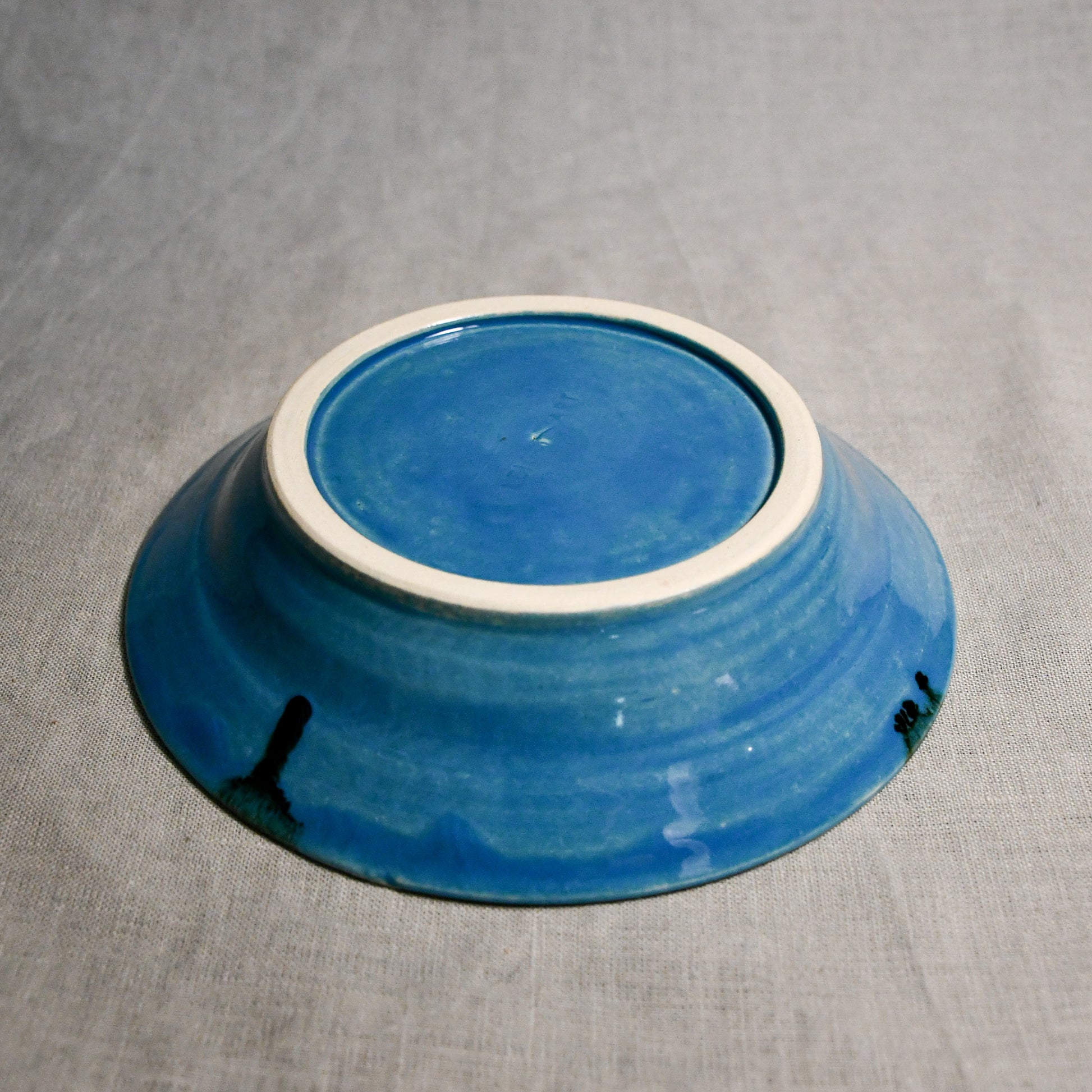 Close up of bottom of a turquoise ceramic saucer showing exposed stoneware clay foot and texture
