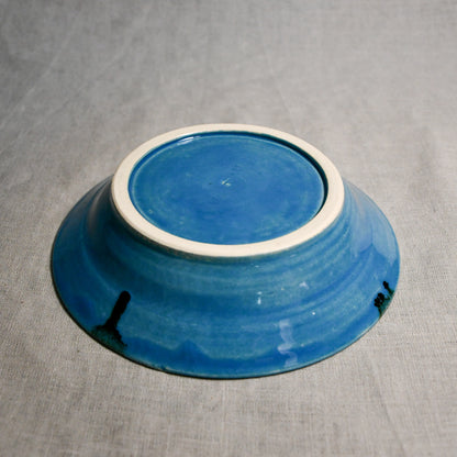 Close up of bottom of a turquoise ceramic saucer showing exposed stoneware clay foot and texture