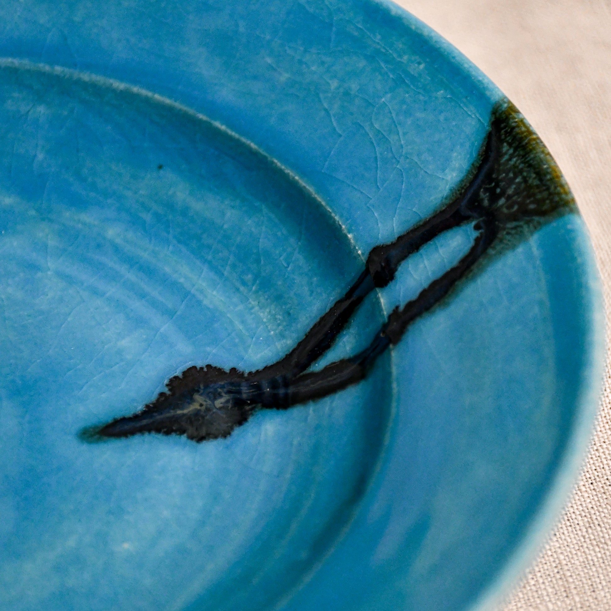 Close up of turquoise handmade wheelthrown pottery saucer with black drips and crazing from the 5th Buffalo collection by Leigh Art